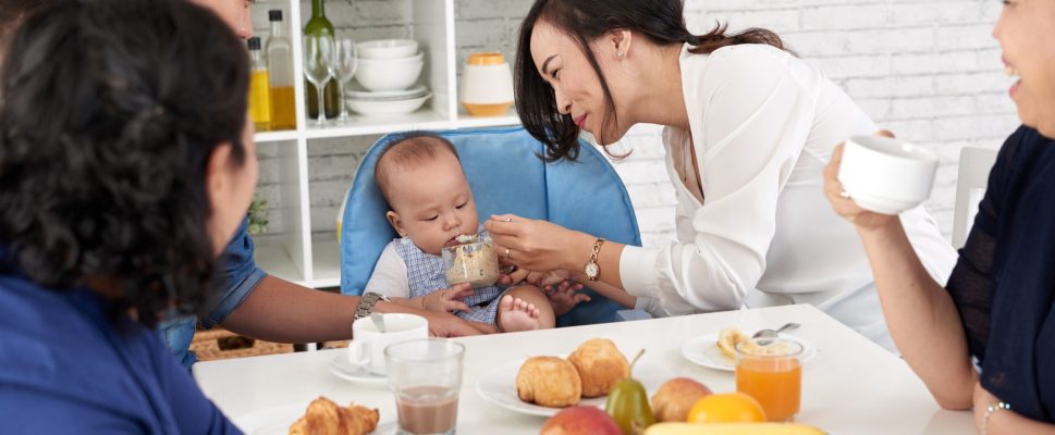 Portrait of happy Asian family at breakfast, mother feeding baby boy at dining table and smiling